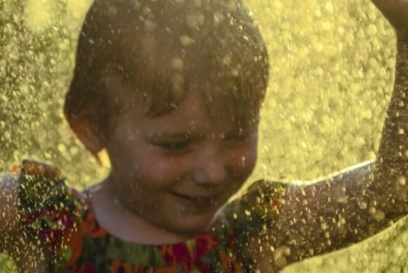Young girl playing in the spray of a garden sprinkler.