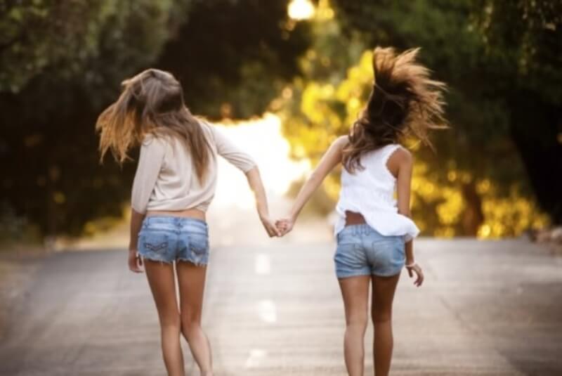 Two young girls walking in middle of the road, holding hands.