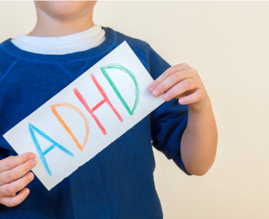 Child in blue top holding up hand drawn sign that says ADHD