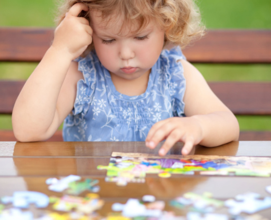 Little girl with blond curly hair having trouble with a puzzle
