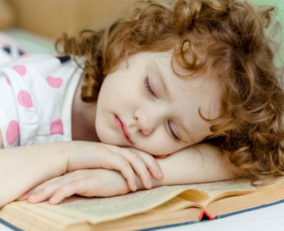 Little girl with curly red hair has fallen asleep on her book.